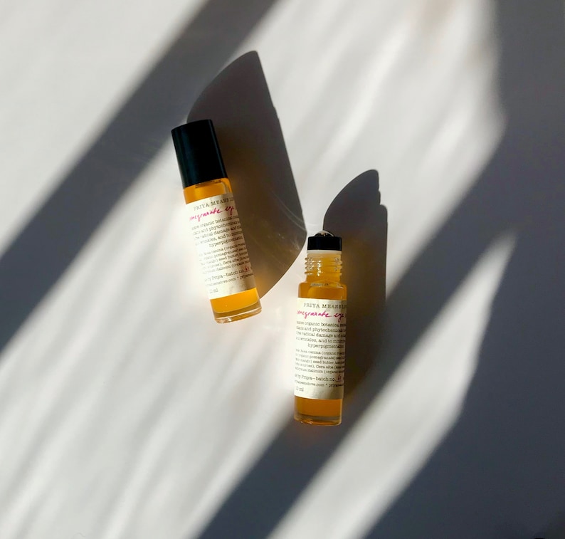 May include: Two small amber glass bottles with rollerball applicators. The bottles are labeled "Priya Meanley - pomegranate eye serum".
