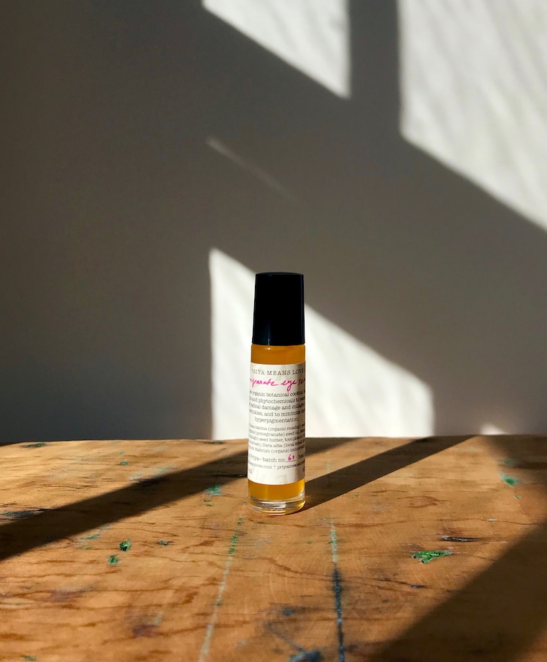 May include: A small amber glass bottle with a black roller top. The bottle is labeled "pomegranate eye serum" and contains organic botanical extracts, antioxidants, and phytochemicals to help reduce the appearance of dark circles, puffiness, and fine lines.