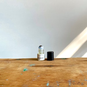 May include: A clear glass roller bottle with a silver roller ball and a black cap. The bottle is labelled "GUNSMOKE" with the text "WITH VITAMIN E OIL" underneath.