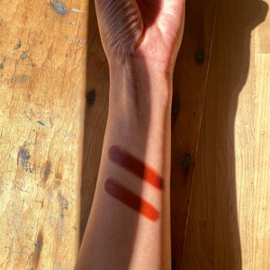 K&ouml;nnte beinhalten: Zwei Farbmuster in einem tiefen Rotbraun auf dem Arm einer Person. Die Muster liegen nebeneinander und sind leicht unterschiedlich.