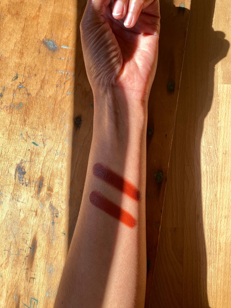 K&ouml;nnte beinhalten: Zwei Farbmuster in einem tiefen Rotbraun auf dem Arm einer Person. Die Muster liegen nebeneinander und sind leicht unterschiedlich.