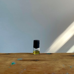 May include: A small glass bottle with a black cap, filled with a yellow liquid, sits on a wooden surface.