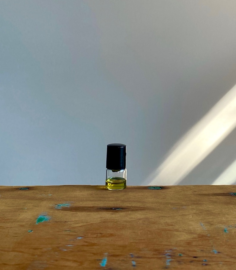 May include: A small glass bottle with a black cap, filled with a yellow liquid, sits on a wooden surface.