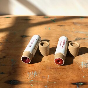 May include: Two brown cardboard tubes with red lip balm inside. The tubes are labeled "Lip Therapy" and "Ocher Lip Therapy".