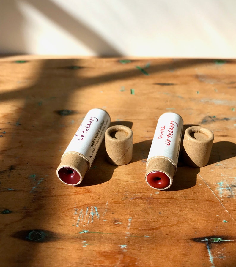 May include: Two brown cardboard tubes with red lip balm inside. The tubes are labeled "Lip Therapy" and "Ocher Lip Therapy".