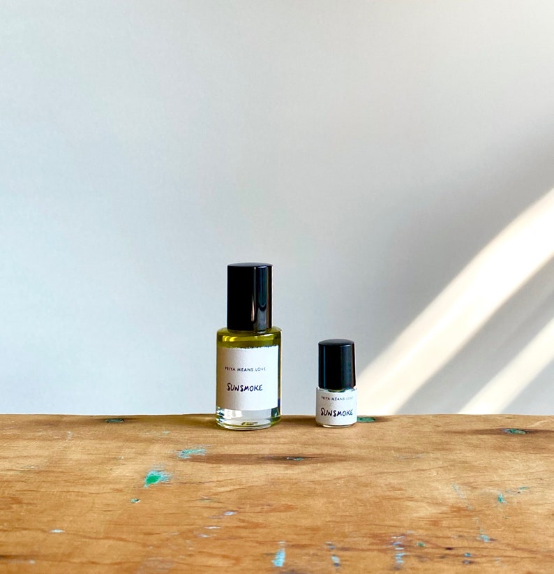 May include: Two glass bottles of perfume with black caps and white labels. The larger bottle says "PETA MEANS LOVE SUNSMOKE" and the smaller bottle says "PETA MEANS LOVE SUNSMOKE". The bottles are on a wooden surface.