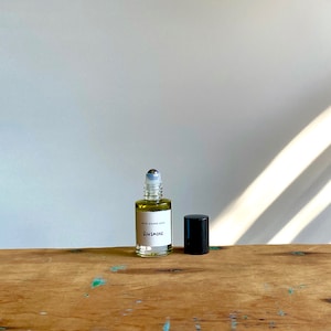 May include: A clear glass roller bottle with a black cap and a white label that reads "PETA MEANS LOVE SUNSMOKE". The bottle is sitting on a wooden surface.