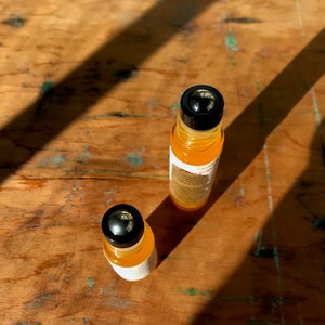May include: Two amber glass roller bottles with black caps and silver roller balls. The bottles are on a wooden surface.