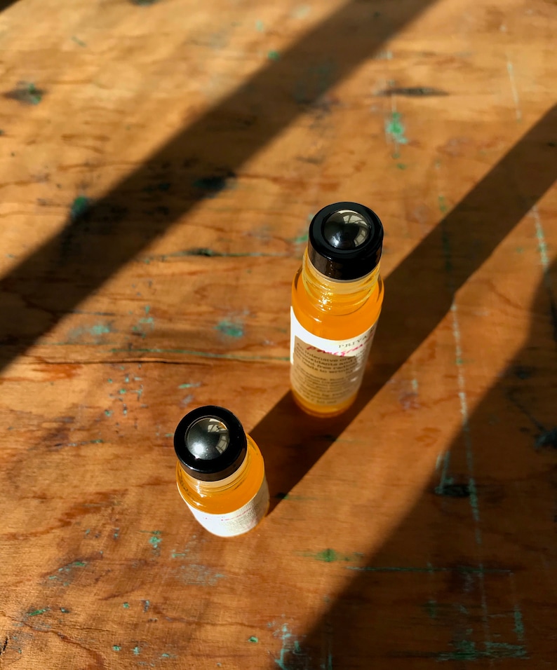 May include: Two amber glass roller bottles with black caps and silver roller balls. The bottles are on a wooden surface.