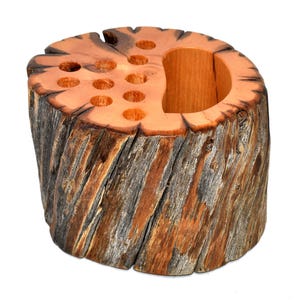 May include: A wooden pencil holder shaped like a tree stump with multiple holes for pencils and a larger hole for pens. The wood is a natural brown color with gray streaks.