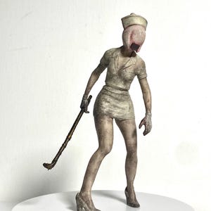 May include: A figurine of a nurse wearing a short, stained uniform and a cap, with a featureless, fleshy head and a dark rectangular mouth. The figure stands in a hunched pose, holding a long, thin, dark brown rod in one hand while wearing heels.