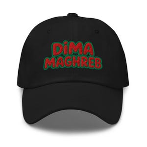 May include: A black baseball cap featuring the embroidered text DIMA MAGHREB in red letters with a green outline. The cap has a structured crown, a curved brim, and a button on top. The embroidery is centered on the front panel of the hat.