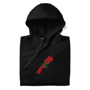 May include: Black hooded sweatshirt featuring a red embroidered outline of the Moroccan map with a green star in the center. The hoodie has a drawstring and a front pocket. The garment is folded.