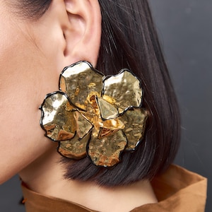 Puede incluir: Grandes pendientes de oro en forma de flor con contornos negros. Los pendientes están hechos de metal texturizado y tienen un diseño tridimensional.