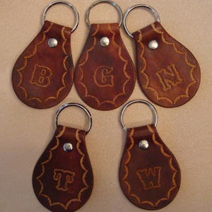 May include: Five brown leather keychains with silver key rings. Each keychain has a different letter embossed on it: B, G, N, T, and W.