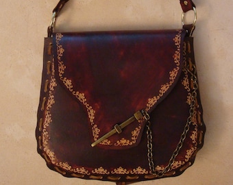 Peut inclure: Un sac à main en cuir marron avec une fermeture à rabat et une chaîne décorative. Le sac a un fermoir en métal doré et des broderies florales complexes autour des bords.