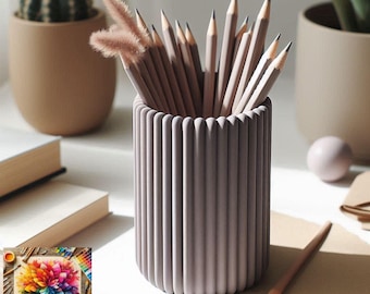 May include: A cylindrical, ribbed, mauve pencil holder filled with sharpened pencils. The pencils are light brown with black tips. A small cactus in a tan pot and a book are in the background. A colorful palette is in the lower left corner.