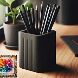 May include: A black pencil pot containing several black pencils with sharpened tips. A colourful floral painting and a small potted plant are also visible. The items are arranged on a wooden surface, creating a workspace scene.