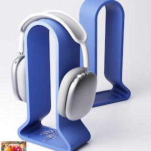 May include: Two blue headphone stands with a modern design. One stand holds silver and white headphones. The stands have a curved, arched shape and a textured surface. Paper clips are on the base of the stand.