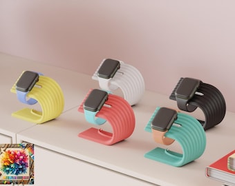 May include: A collection of colorful watch stands in yellow, white, coral, black, and teal. Each stand holds a smartwatch with a matching band. The stands are on a white surface with a pink background.