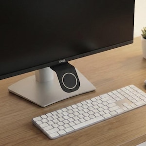 May include: A contemporary desk arrangement with a black Dell monitor, a silver keyboard, and a wireless mouse. A small succulent plant in a white pot is on the right. The desk is made of light-coloured wood.