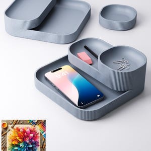 May include: A collection of light blue desk tidies with a ribbed texture. The set includes a large tray, a smaller tray, and two small round containers. A smartphone, pencil, eraser, and paper clips are inside the organisers.