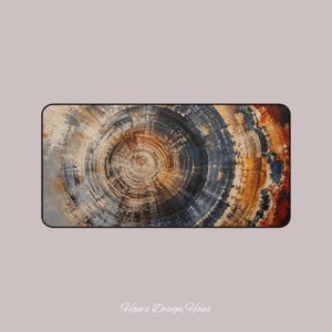 May include: A rectangular desk mat featuring a high-resolution print of a tree ring cross-section. The design displays concentric circles in shades of deep charcoal, warm amber, burnt orange, and cream. The text Hope's Design Haus is visible.