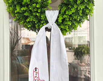 May include: A white door scarf with a red and black embroidered cowboy boot design and the text "Go Sack!" is hanging on a door with a green wreath.
