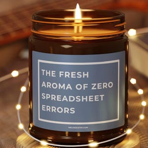 Op de afbeelding: Een brandende kaars in een bruine glazen pot met een blauw etiket met de tekst "THE FRESH AROMA OF ZERO SPREADSHEET ERRORS". De kaars staat op een houten onderzetter, omringd door lichtslingers.
