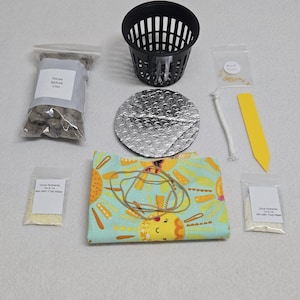 May include: Hydroponic growing kit with a black plastic basket, a silver foil lid, and a colorful fabric wrap. Includes a bag of growing medium, plant food, and other accessories. The fabric wrap has a yellow and orange sunflower design.