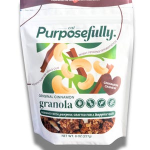 May include: A white packet of "Purposefully" original cinnamon granola. The packet features a graphic of cashews and cinnamon sticks. Text includes "Cinnamon Cashew", "Gluten Free", and "Net Wt. 227g".