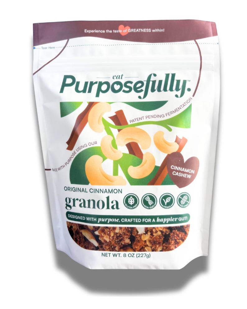 May include: A white packet of "Purposefully" original cinnamon granola. The packet features a graphic of cashews and cinnamon sticks. Text includes "Cinnamon Cashew", "Gluten Free", and "Net Wt. 227g".
