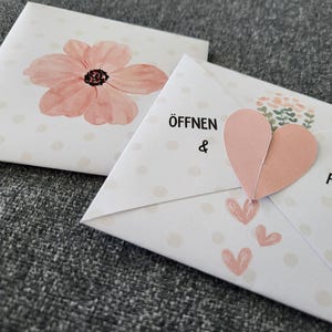 May include: Two white envelopes with pink polka dots. The top envelope has a pink watercolour flower. The bottom envelope has a pink heart and the text "ÖFFNEN & FREUEN".