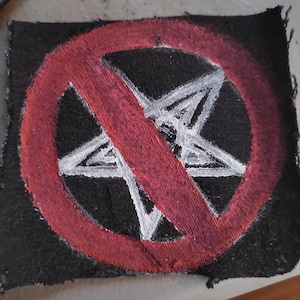 Peut inclure: Un écusson noir avec un pentagramme blanc barré d'un cercle et d'une barre rouges. L'écusson est rectangulaire avec des bords effilochés. Le pentagramme est dessiné à la main avec un contour blanc.