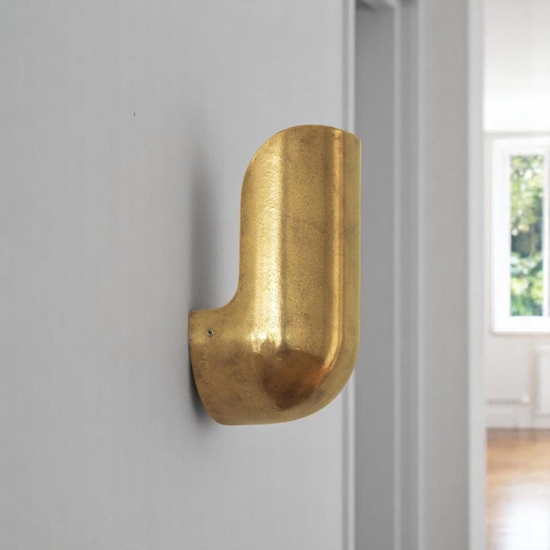 May include: A gold-colored wall-mounted light fixture with a curved design. The fixture is made of metal and has a textured surface.