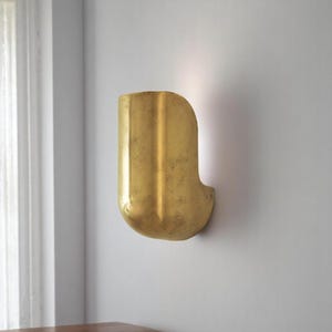 May include: A gold-colored wall sconce with a curved, rectangular shape. The sconce has a textured surface and is mounted on a white wall.