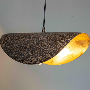 Può includere: Lampada a sospensione dal design unico. L'esterno è marrone scuro con un motivo maculato, mentre l'interno è dorato. La lampada è appesa a un cavo nero.