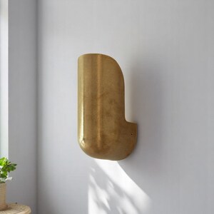 May include: A brass wall sconce with a curved, rounded shape. The sconce has a textured, hammered finish.