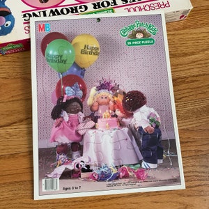 May include: A 25-piece Cabbage Patch Kids puzzle featuring a birthday party scene with four dolls, a cake, and balloons. The puzzle is designed for ages 3 to 7. The box has a pink and blue background with the words "Preschool's for Growing" and "Sesame Street Preschool" on it.