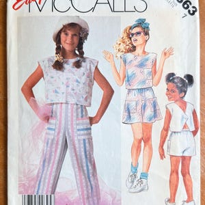 May include: Vintage McCall's sewing pattern for girls' clothing, featuring illustrations of three outfits. The outfits include a crop top and striped pants, a matching top and shorts set, and a white shorts set. The pattern cover is white with red and black text.
