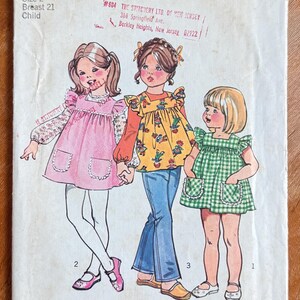 May include: Vintage Simplicity sewing pattern 5479 for a child's dress, top, and pants. The cover features illustrations of three children wearing the garments. The pattern includes size 2 with a 21-inch breast measurement.