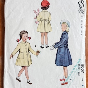 May include: Vintage McCall's printed pattern for a child's coat, featuring illustrations of three children in different coat designs. The pattern includes the number 8007 and the size 2. The cover is off-white with a worn appearance.