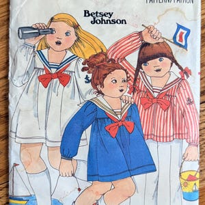 May include: Vintage Butterick sewing pattern featuring three children in sailor-themed outfits. The illustration includes a white dress with a red bow, a blue dress, and a red and white striped shirt. The pattern is size 3 and designed by Betsey Johnson.