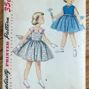 May include: Vintage Simplicity sewing pattern for a girl's dress. The pattern is for size 4 and costs 35 cents. The pattern shows two girls wearing dresses, one in a blue and white gingham pattern and the other in a floral print.