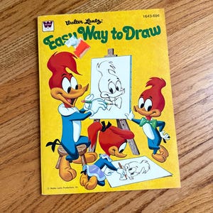 May include: A vintage "Easy Way to Draw" book featuring Woody Woodpecker and friends. The cover is yellow with the title in green and illustrations of the cartoon characters drawing. The book has a vintage aesthetic.