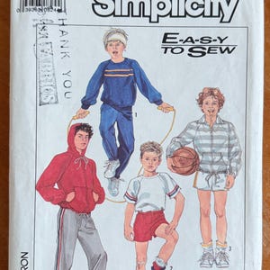 May include: Simplicity sewing pattern featuring illustrations of children in athletic wear. The pattern includes a blue tracksuit, red hoodie with gray pants, a white t-shirt with red shorts, and a striped jacket with shorts. The text "E-A-S-Y TO SEW" is visible.