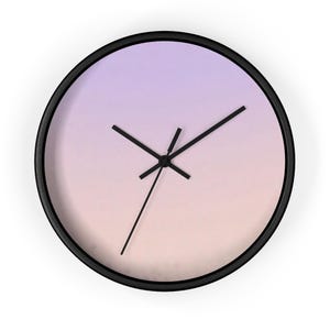 May include: Round wall clock with a black frame and a gradient face in shades of purple and peach. The clock features black hands indicating the time. A decorative piece for any room.