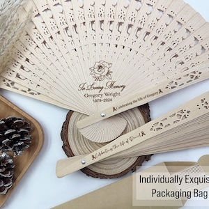 May include: A wooden folding fan with a white background and black text that reads "In Loving Memory Gregory Wright 1979-2024 Celebrating the life of Gregory". The fan is closed and has a decorative design.