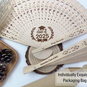 May include: Wooden graduation fans with intricate cut-out designs. One fan displays "Class of 2025" and personalized text. The image includes a stack of fans, packaging, and decorative elements. The fans are light brown.