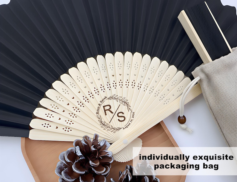 May include: A black and white folding fan with a wooden handle, personalized with initials and a date. The fan is in a beige drawstring bag, with the text "individually exquisite packaging bag".